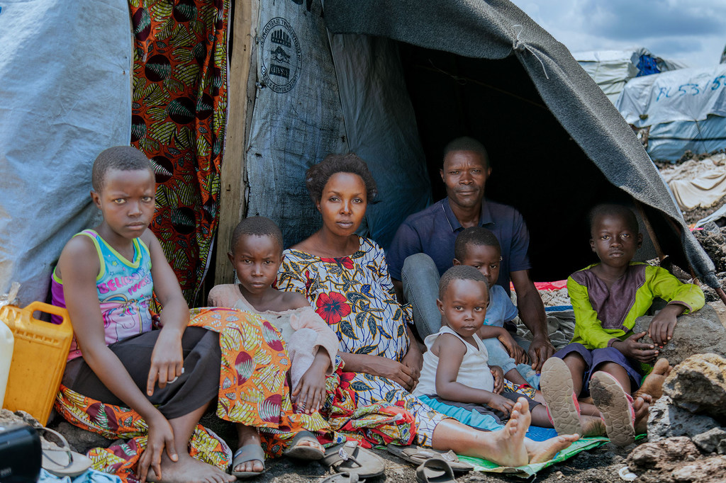 Ombeni, her husband, and their children gather outside their makeshift shelter at a displacement site west of Goma after fleeing violence.